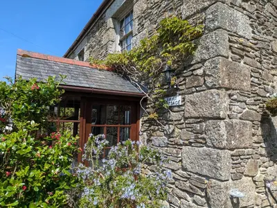 an old stone building with a window and flowers at Swift Cottage in Mawgan