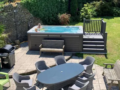 a child in a hot tub with a table and chairs at Polean Farm Old Farmhouse - With Large Jacuzzi, Games Room, Near the Sea and with Free Access to a Nearby Pool in Looe