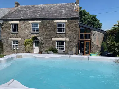 a house with a large swimming pool in front of a house at Polean Farm Old Farmhouse - With Large Jacuzzi, Games Room, Near the Sea and with Free Access to a Nearby Pool in Looe