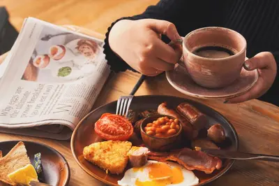 a person holding a cup of coffee next to a plate of breakfast food at The Old Custom House in Padstow
