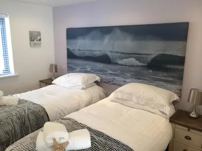 two beds in a room with a large painting on the wall at 9 Sandpiper Cottages in Newquay
