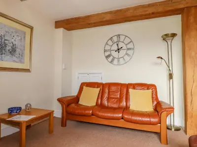 a brown leather couch in a living room with a clock on the wall at Wheal Honey in Newlyn East
