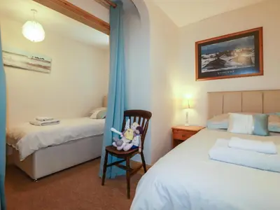 a bedroom with two beds and a chair and a mirror at Summerfield Cottage in Gorran Haven