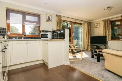 a kitchen with white cabinets and a living room at Silverwell Forge in Chacewater