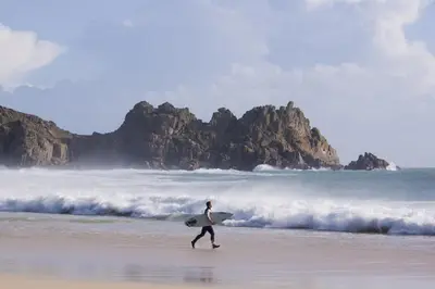 a man walking on the beach with a surfboard at Cargurra Park Farm in Boscastle