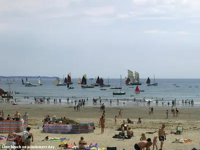 a group of people on a beach with boats in the water at Sand Dune in Looe