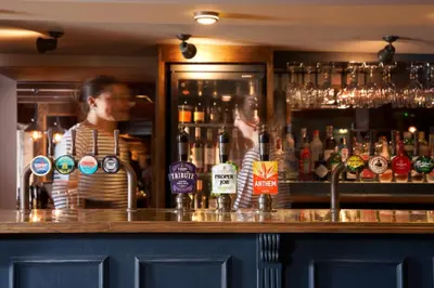 a woman standing behind a bar with a bartender at Harbour Inn in Porthleven