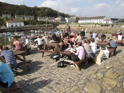 a group of people sitting at picnic tables by the water at Harbour Inn in Porthleven
