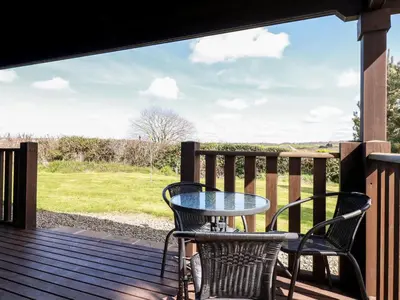 a table and chairs on a deck with a view of a field at Maple Lodge in Bodmin