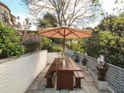 a wooden picnic table with an umbrella on a fence at Sea Cliff Cottage in Pentewan