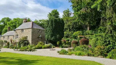 an old stone house with a garden in front of it at The Hideaway & Spa Terrace at Tregoose Old Mill in Newquay