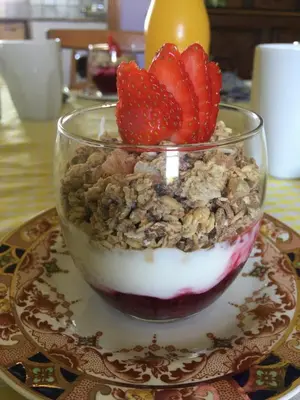 a bowl of yogurt with strawberries and granola on a plate at Treganoon House, Lanlivery in Bodmin