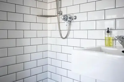 a white tiled bathroom with a shower and a sink at The Olde Malthouse Inn in Tintagel