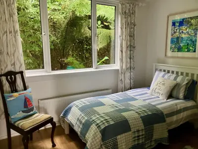 a bedroom with a bed and a chair and a window at Fuchsia Cottage in Porthallow