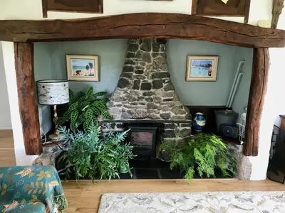 a living room with a stone fireplace in the corner at Fuchsia Cottage in Porthallow