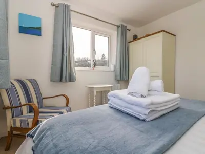 a bedroom with a bed and a chair and a window at Cockle Island Cottage in Porthallow