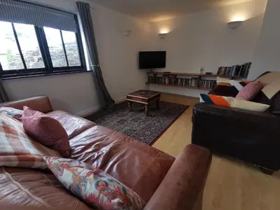 a living room with a leather couch and a tv at THE OLD RECTORY ROSE COTTAGE in Jacobstow 10 mins to Widemouth bay and Crackington Haven,Nearby Bude,Tintagel,Port Issac,Clovelly,PARKING FOR LARGE AND MULTIPLE VEHICLES in Jacobstow
