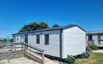 a white tiny house with a wooden deck at Polborder Holidays Looe Country Park in Looe