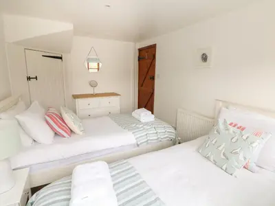 two beds in a room with white walls at Erin Cottage in Pelynt