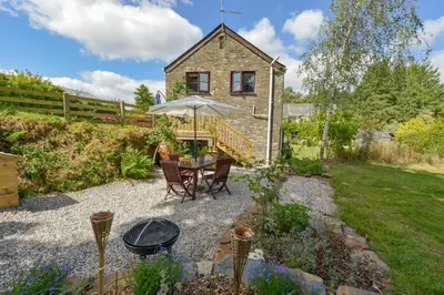 a patio with a table and an umbrella in a garden at Erin Cottage in Pelynt