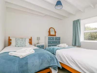 two beds in a white room with a window at The Barn in Gunwalloe