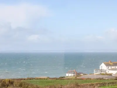 a house on a hill with the ocean in the background at The Barn in Gunwalloe