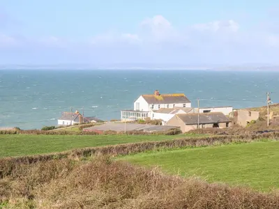 a large white house on a hill near the ocean at The Barn in Gunwalloe