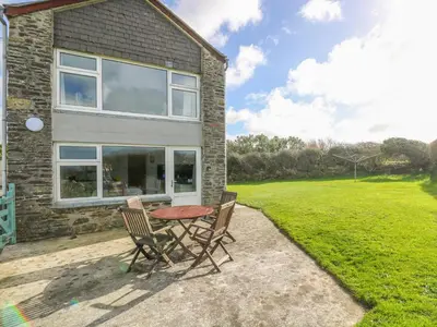 a patio with a table and chairs in front of a house at The Barn in Gunwalloe
