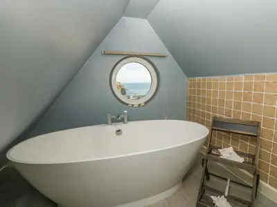 a bathroom with a large white tub in a attic at Trelawns in Mawgan Porth