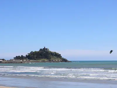 a bird flying over a beach with an island in the ocean at Seashells in Marazion