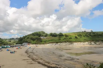a beach with a group of people sitting on the sand at Pugwash Cottage in Falmouth