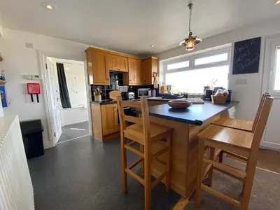 a kitchen with wooden cabinets and a island with chairs at THE PENTHOUSE Top Floor Apartment with Bay Views, Large Balcony & Onsite Parking in St Ives