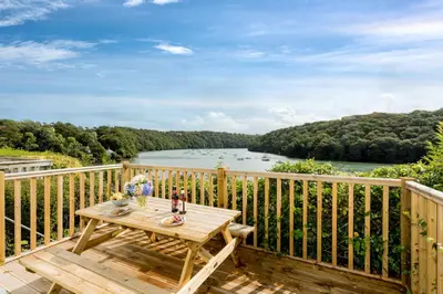 a wooden deck with a table and a view of a river at Fal River Cottage in Truro