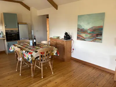 a dining room with a table and a kitchen at The Byre in Porthtowan