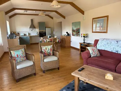 a living room with a couch and chairs and a kitchen at The Byre in Porthtowan