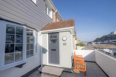 a house with a white door and a wooden chair at Inner Harbour Cottage in Portreath