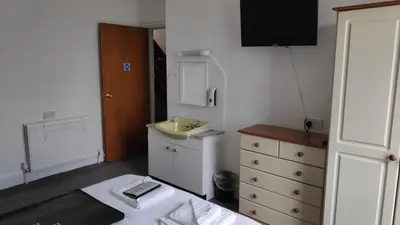 a small bedroom with a sink and a dresser at Elnor Guest House in Liskeard