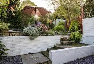 a garden with a brick wall with an umbrella at Porthgwidden Cottage in Uny Lelant