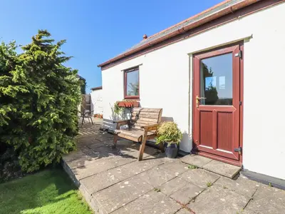 a house with a wooden door and a bench at Bowling Green Cottage in Redruth