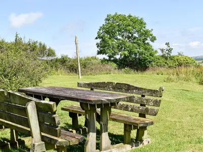 a wooden picnic table and two benches in a field at Round House - Uk12083 in Saint Endellion