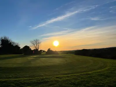 a sunset on a golf course with the sun setting at Wheal Prosper- Beautifully Fitted Wooden Lodge Helston Cornwall in Helston