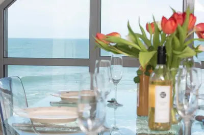 a glass table with a vase of flowers and glasses at Fistral Beach Penthouse, Newquay in Crantock