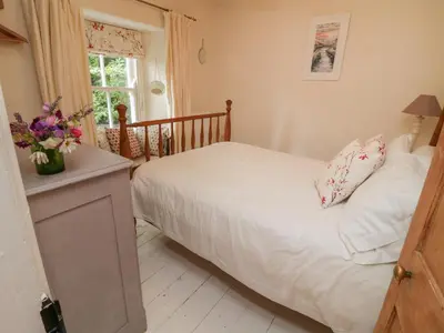 a bedroom with a bed with white sheets and flowers on it at Fairfield Cottage in Boscastle