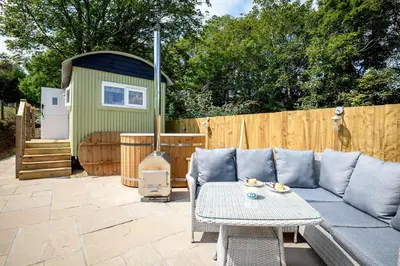 a patio with a couch and a table and a fence at Luxury Coastal Shepherds Hut with hot tub, dining dome & a 5 Minute Walk to Pubs and Village in Polperro