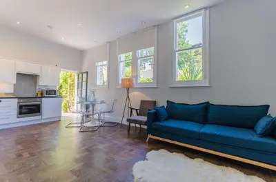 a living room with a blue couch and a kitchen at Luxury Victorian school with views of Harbour in Fowey