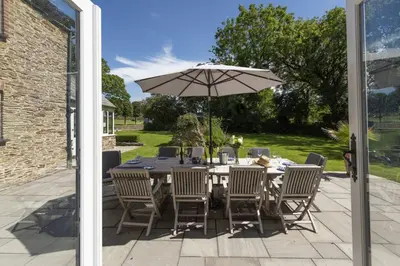a table and chairs with an umbrella on a patio at Mowhay Barn - Woodburner & Hot tub in Padstow