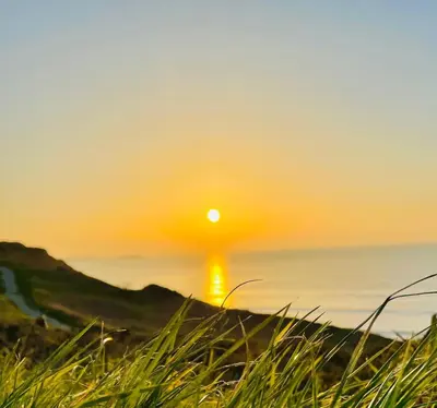 a sun setting over the ocean with grass in the foreground at Newquay Bay Resort - SummerBreeze PV54 in Porth
