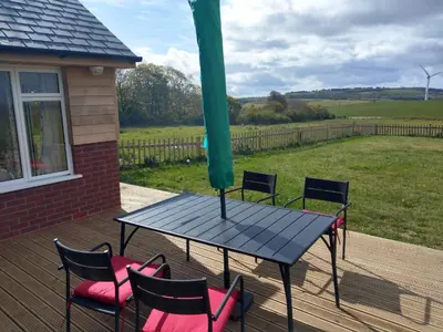 a table and chairs on a deck with a view of a field at Orchard Chalet in Liskeard