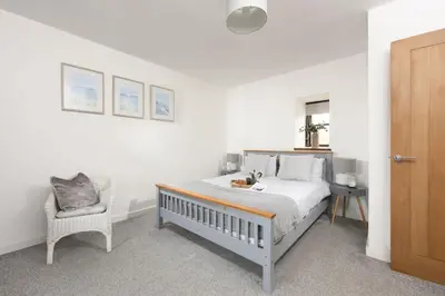 a white bedroom with a bed and a chair at The Old Hay Barn, Hot Tub, Pet Friendly in Ludgvan