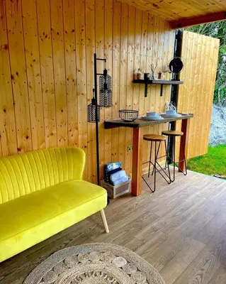 a yellow couch and a bar in a wooden cabin at Trethowels Hidden Huts in St Austell